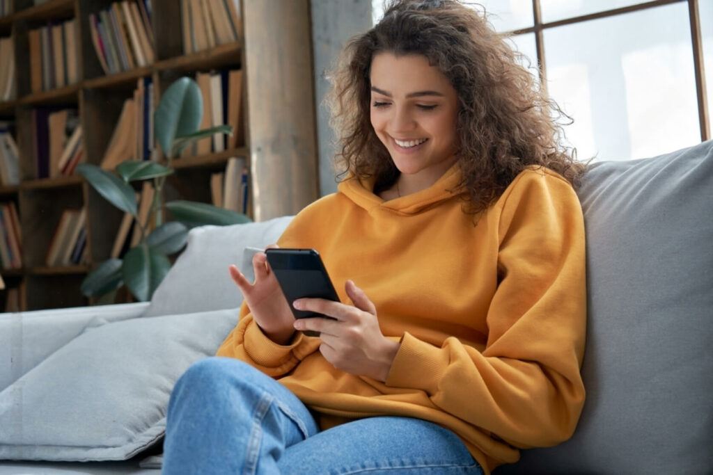 Vrouw zit op de bank met mobiel in haar hand.